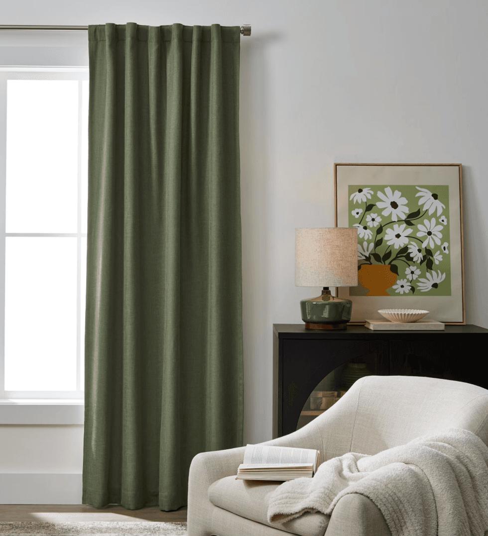 Cozy living room with green curtains, art, lamp, and a chair covered with a book and blanket.