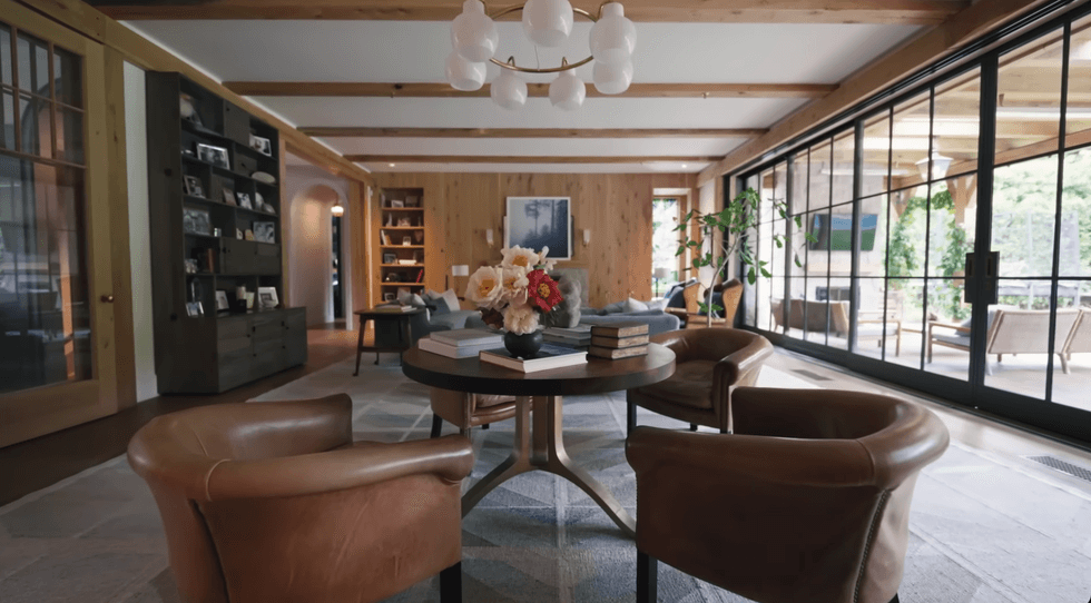 Cozy living room with leather chairs, bookshelves, and large windows overlooking greenery.