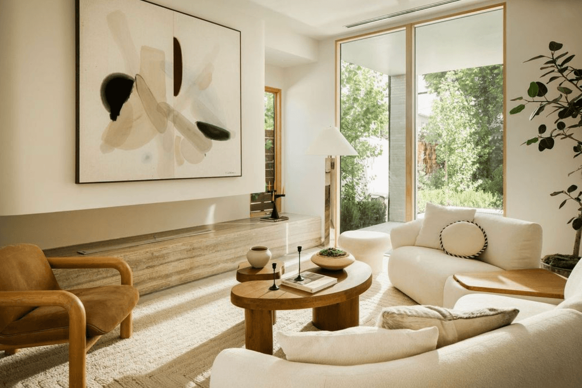 Cozy living room with modern art, light furniture, and large windows showing greenery.