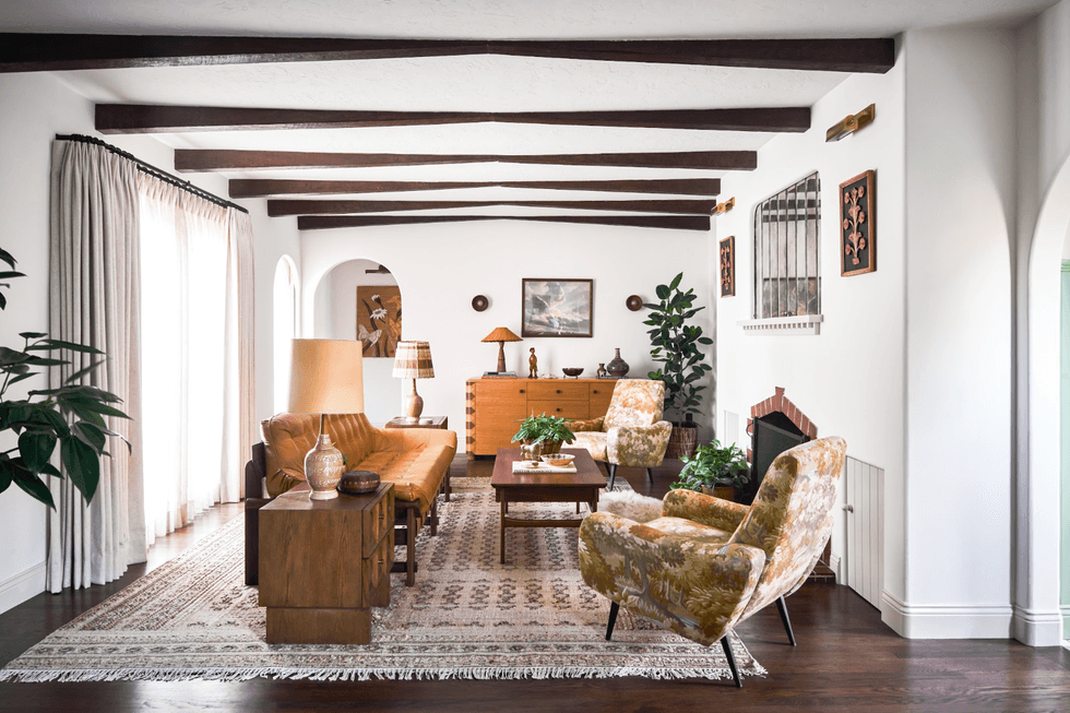 Cozy living room with vintage furniture, exposed beams, and plants on a patterned rug.