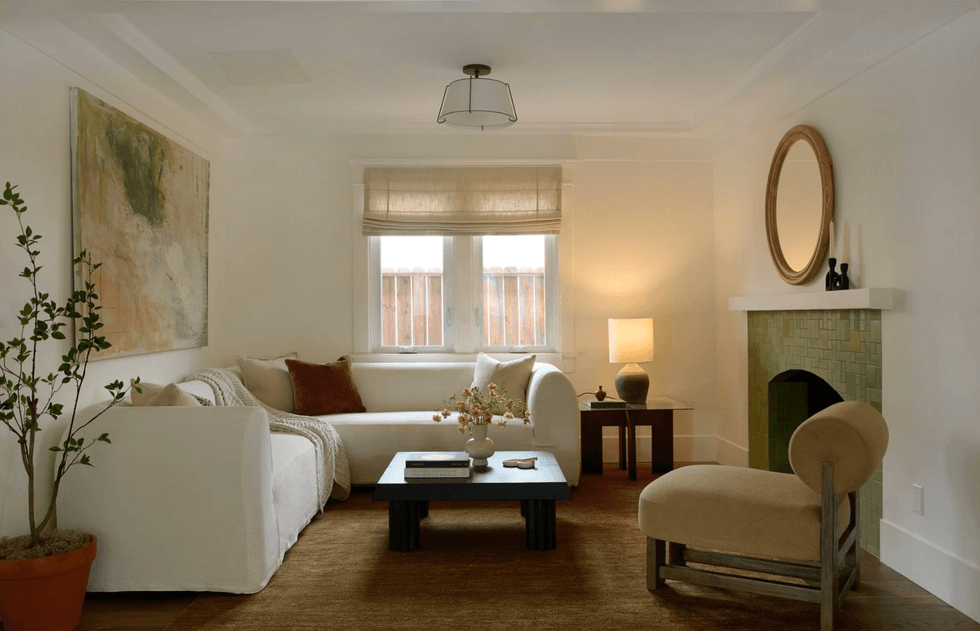Cozy living room with white sofa, armchair, green tiled fireplace, and large artwork on wall.