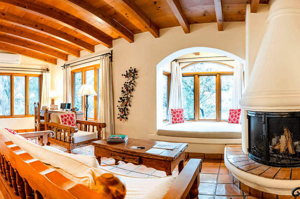 Cozy living room with wooden beams, large windows, and a central fireplace with seating.