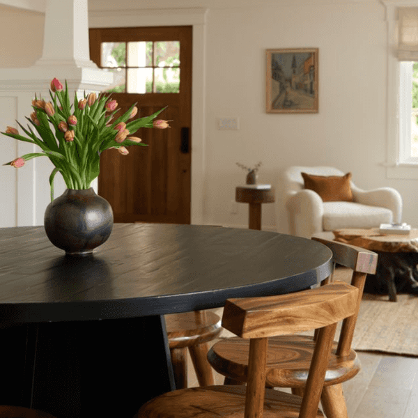 Cozy living space with a black table, tulips, wooden chairs, and a white armchair in the background.