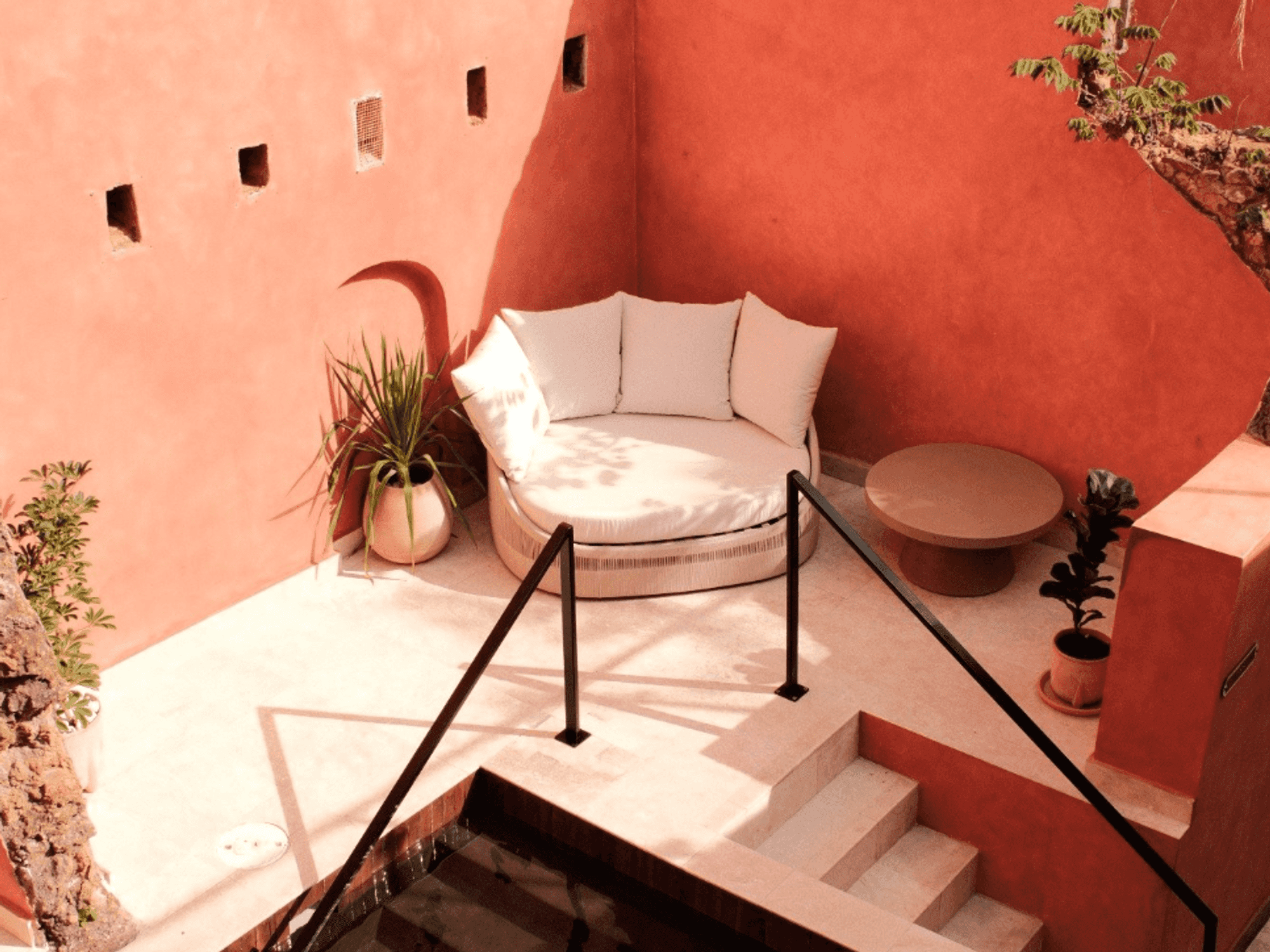 Cozy patio with a round sofa, plants, and orange walls in the sun.