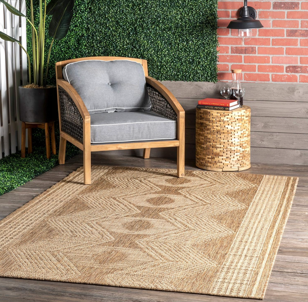 Cozy patio with a wicker chair, patterned rug, and a small side table adorned with decor.