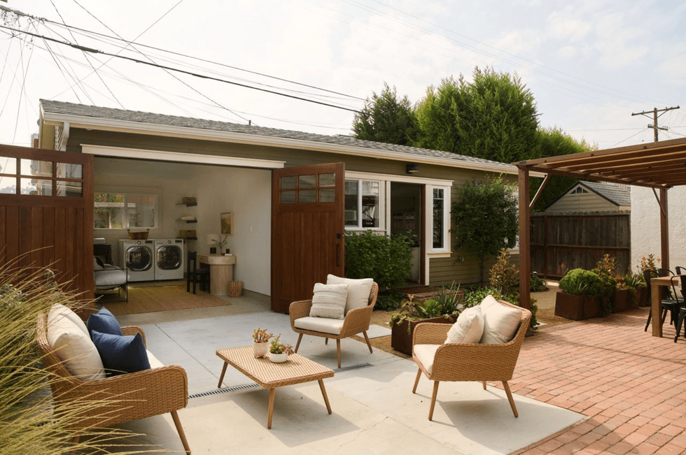 Cozy patio with woven furniture, plants, and an open garage with laundry appliances.