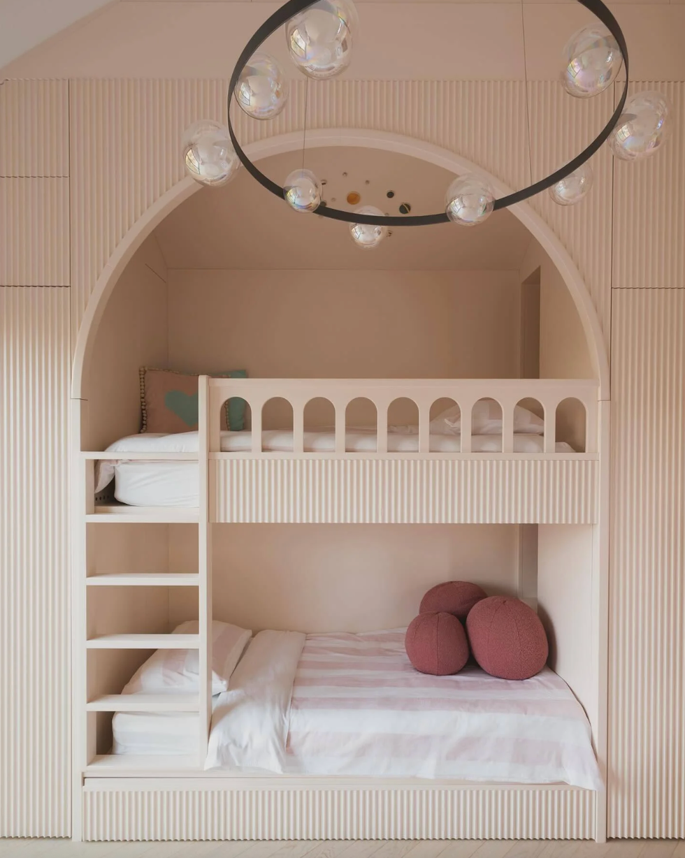 Cozy pink bunk bed with striped bedding and round pillows under a modern chandelier.