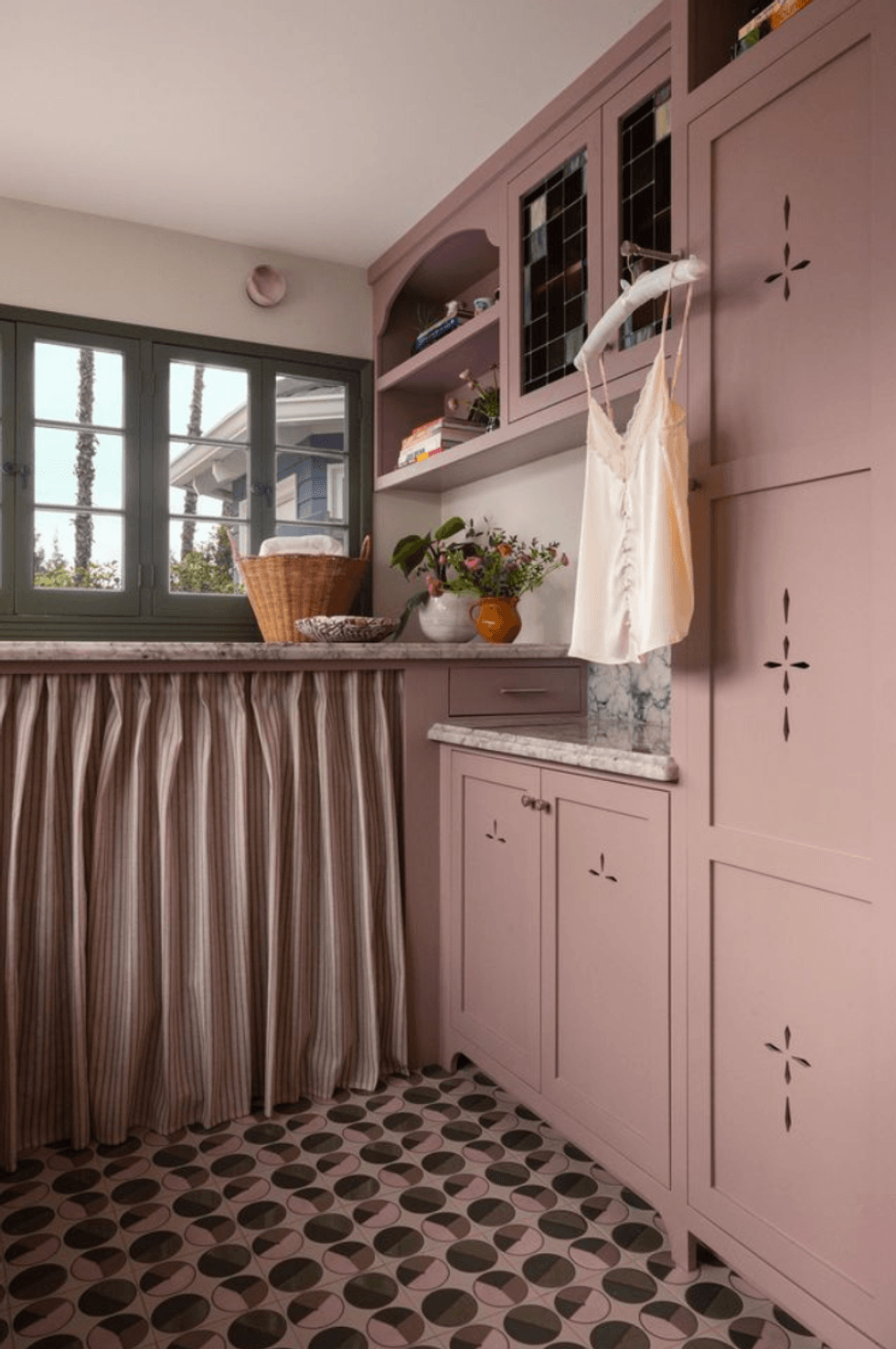 Cozy pink laundry room with cabinets, patterned floor, and a window view.