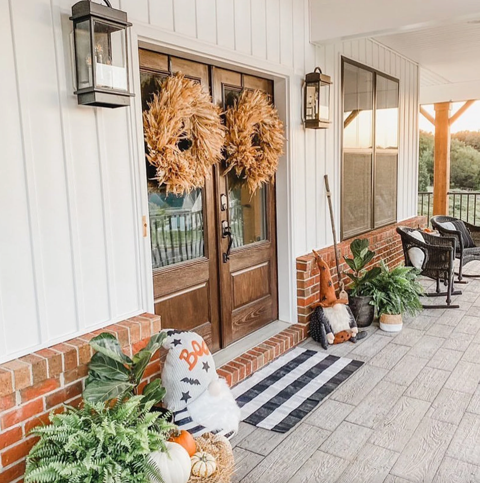 Cozy porch with autumn decor, wreaths, plants, pumpkins, and wicker chairs.