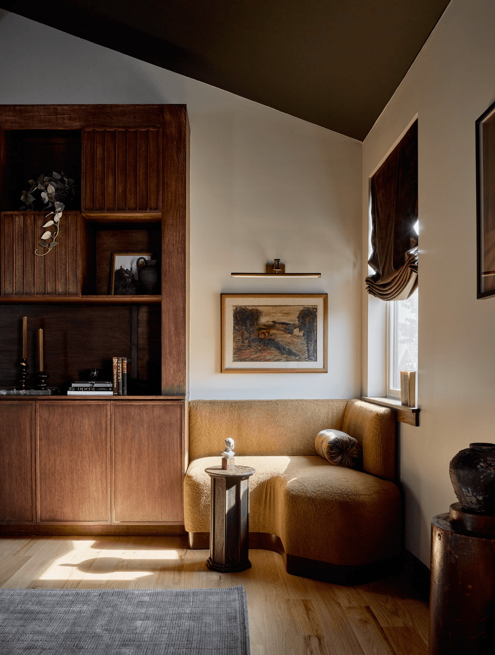 Cozy reading nook with brown couch, shelf, and wall art in a warmly lit room.