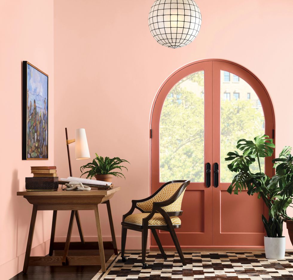 Cozy room with a wooden desk, chair, plants, art, and arched coral doors.