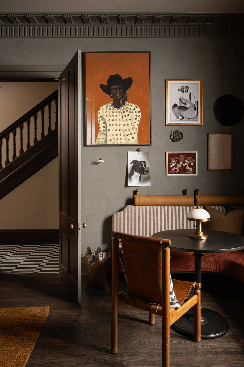 Cozy room with art-filled walls, leather chair, and round table beside a staircase.