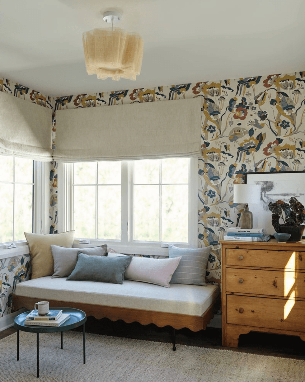 Cozy room with floral wallpaper, daybed, pillows, and wooden dresser near a window nook.