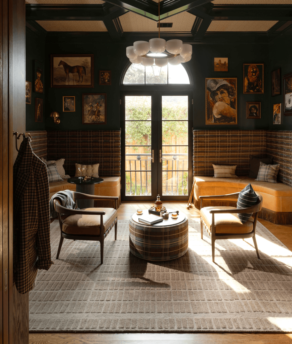 Cozy room with plaid decor, chairs, large window, and framed art on dark walls.