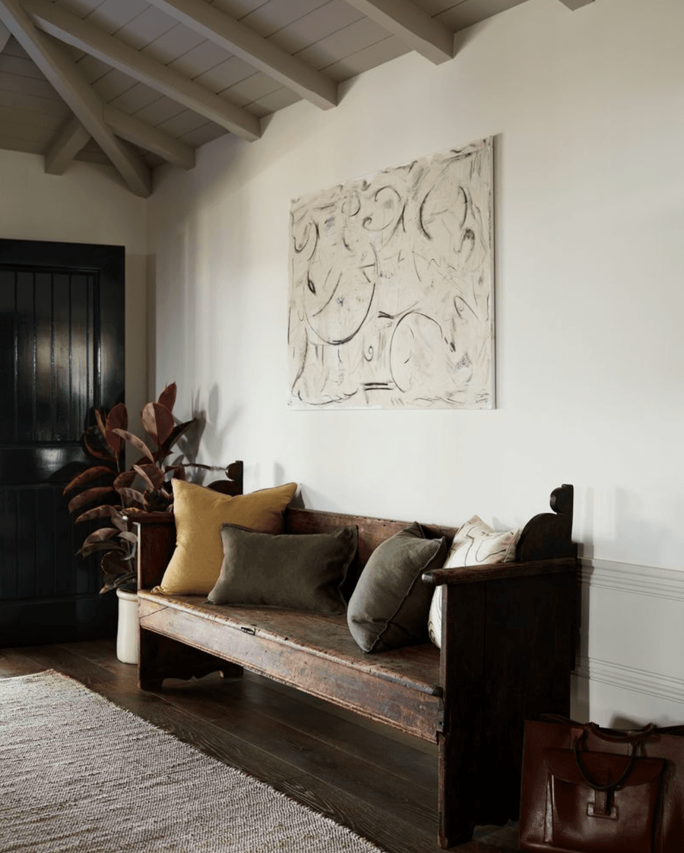 Cozy room with wooden bench, pillows, abstract art, and plant.