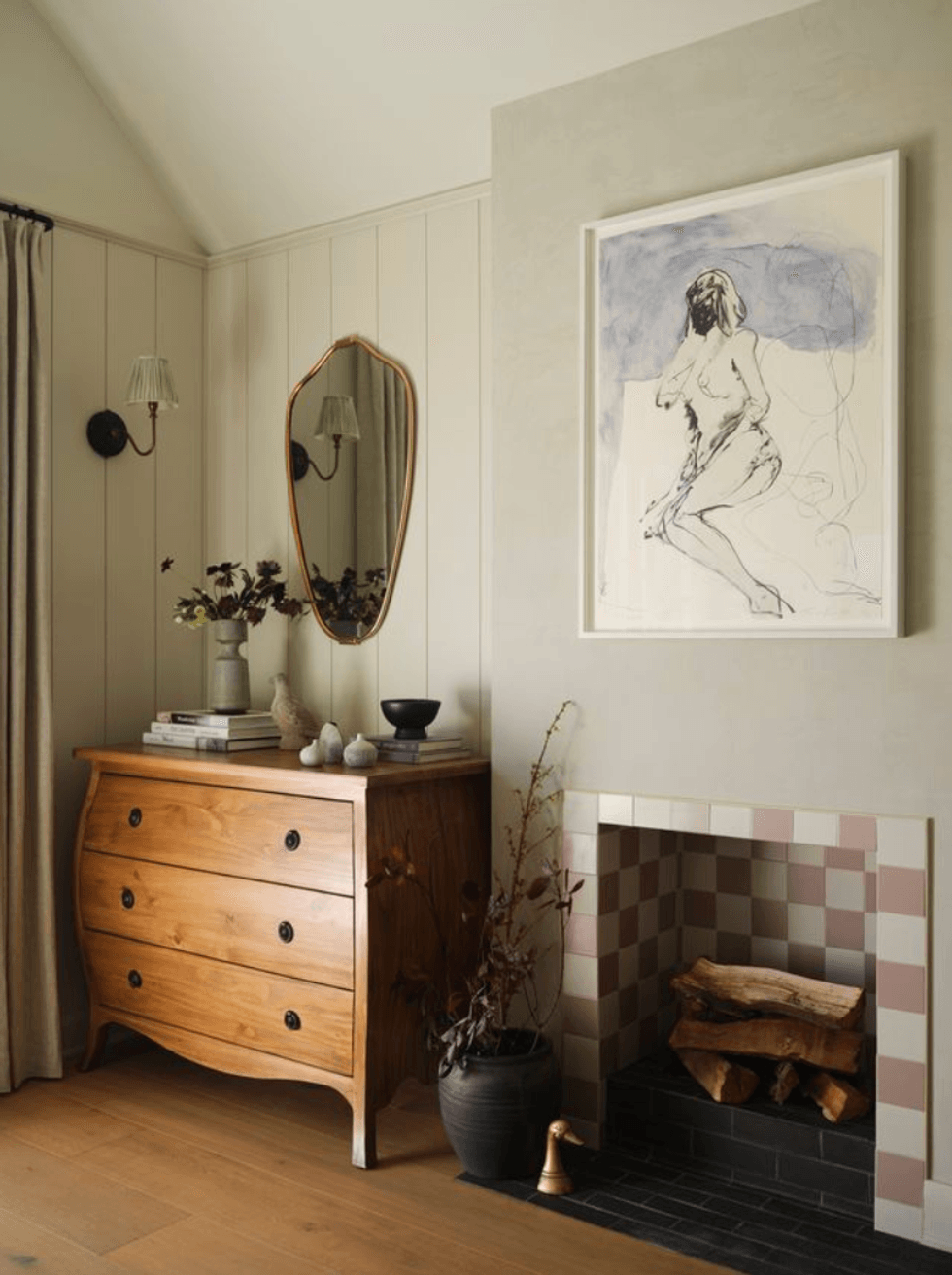Cozy room with wooden dresser, mirror, and framed artwork above a tiled fireplace.