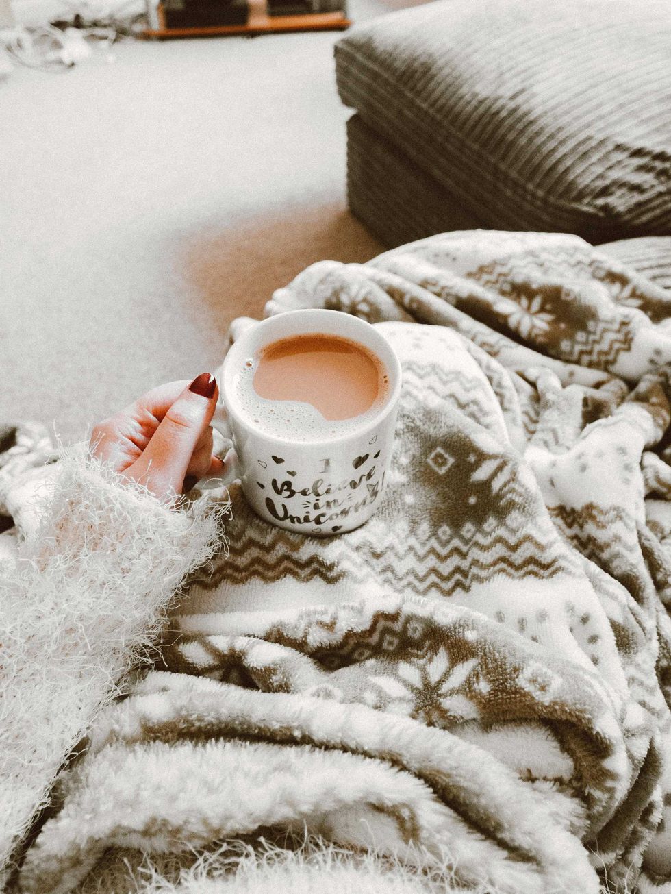Cozy setting with a cup of tea, fluffy sweater, and patterned blanket.