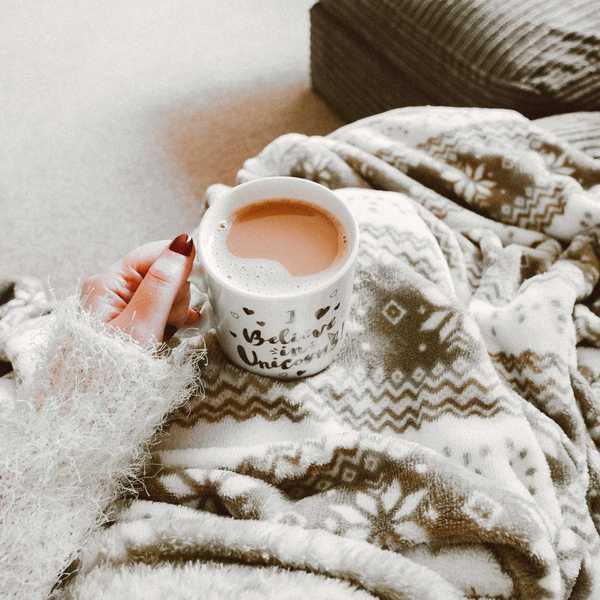 Cozy setting with a mug of tea, patterned blanket, and soft sweater.