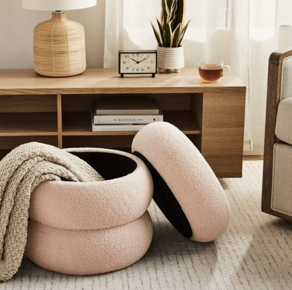 Cozy woven basket with blanket beside a wooden shelf, clock, plant, and a cup of tea.