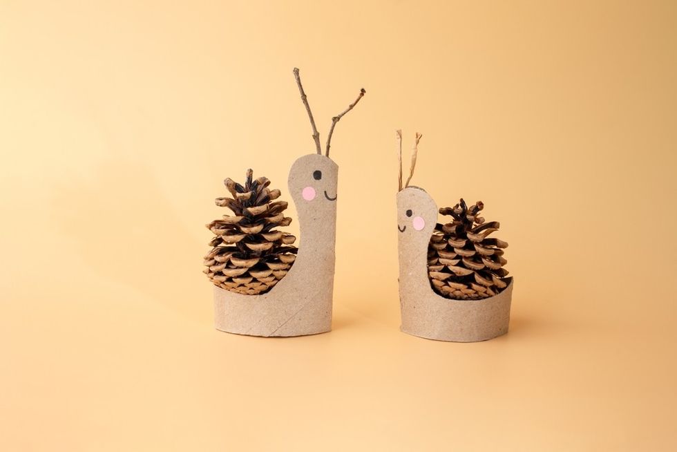 Craft snails made from pinecones and cardboard on a peach background.