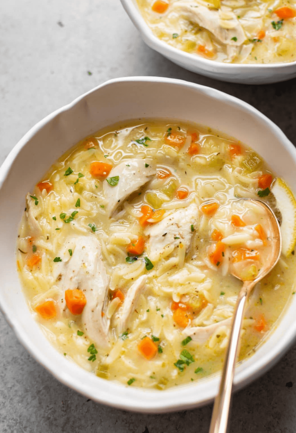 Creamy chicken soup with carrots, noodles, and herbs in a white bowl.