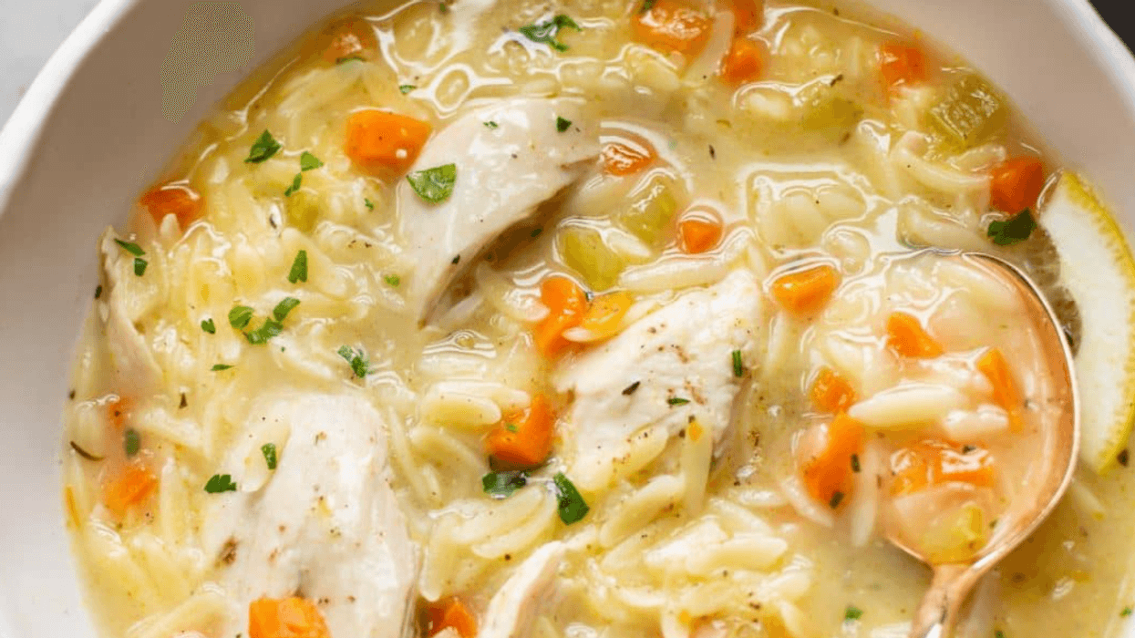 Creamy chicken soup with carrots, noodles, and herbs in a white bowl.