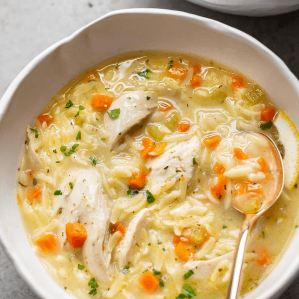 Creamy chicken soup with carrots, noodles, and herbs in a white bowl.