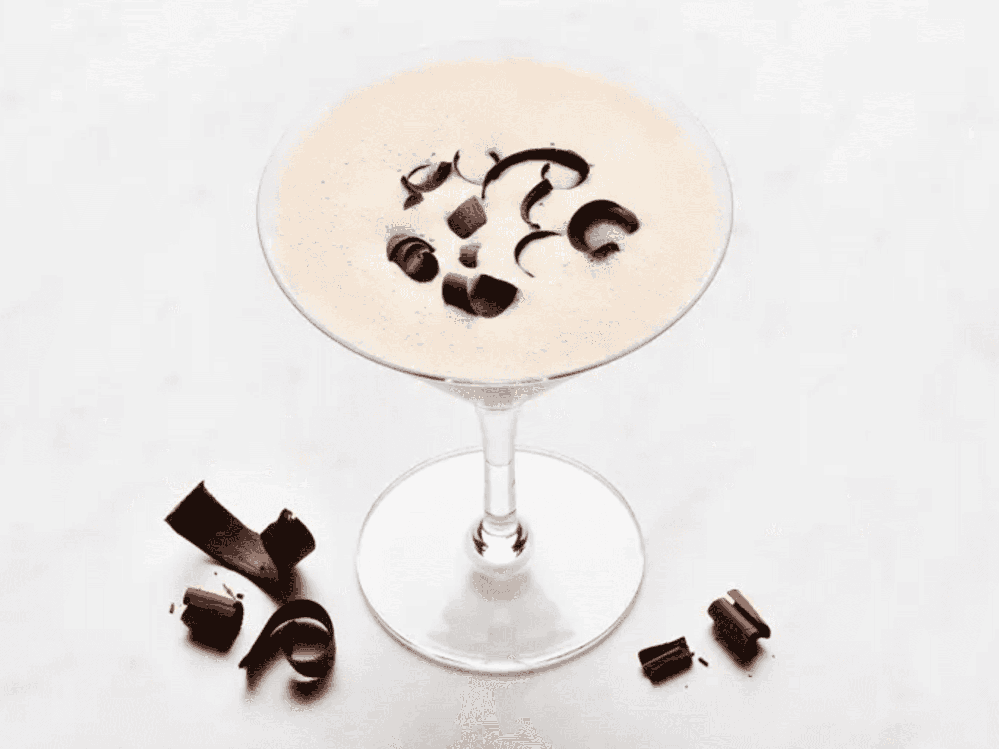 Creamy cocktail topped with chocolate curls in a glass, on a white marble surface.