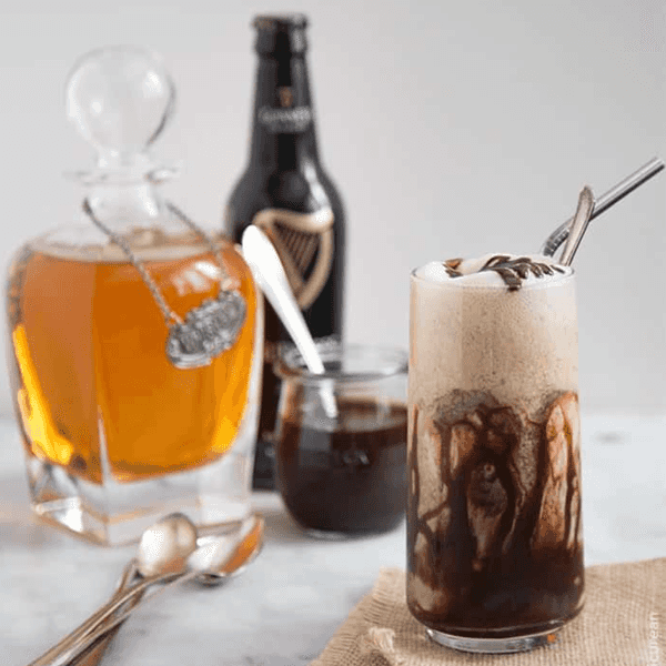 Creamy iced coffee with whiskey and chocolate drizzle on a table with bottles in the background.