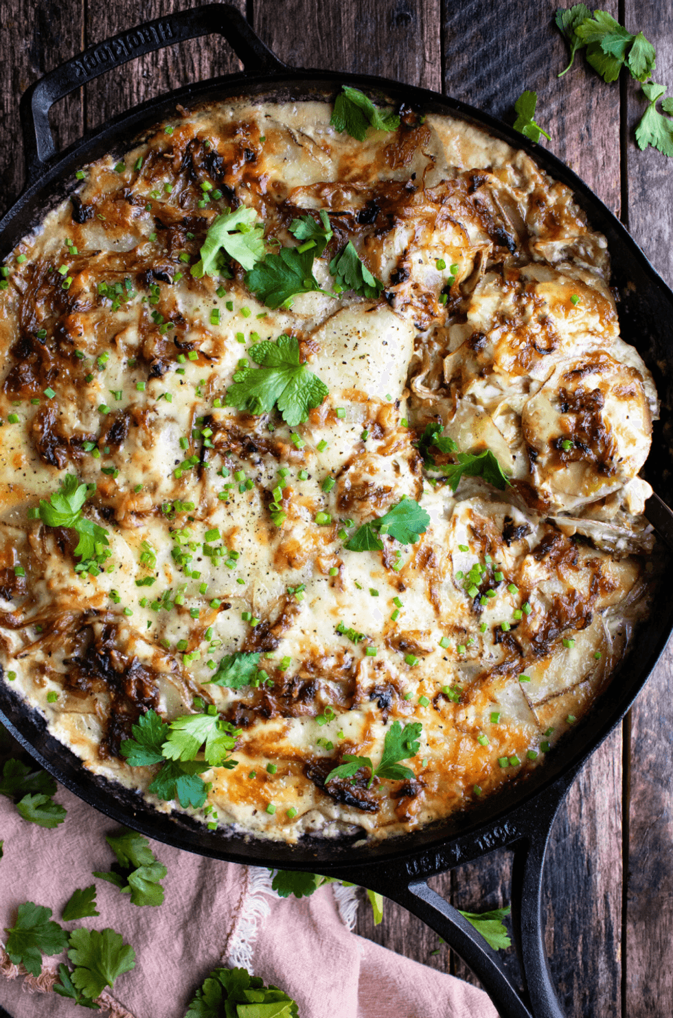 Creamy potato gratin in a skillet, topped with herbs and browned cheese.