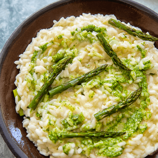 Creamy risotto topped with asparagus and green sauce on a brown plate.