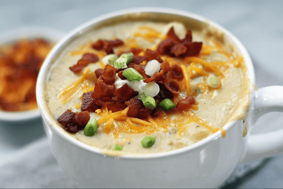 Creamy soup topped with bacon, cheddar, and green onions in a white bowl.