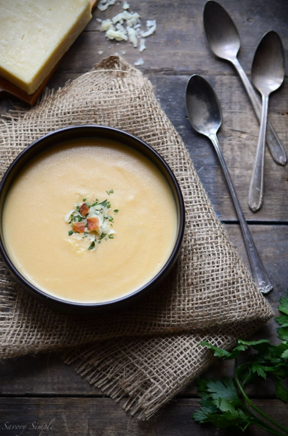 Creamy soup topped with herbs, served on burlap with cheese and spoons.