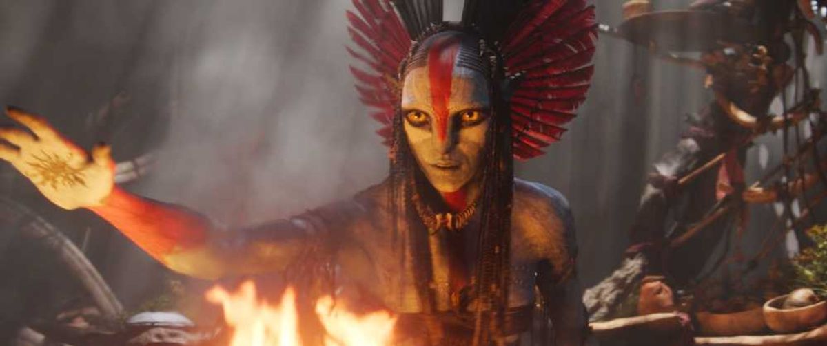 Creature with red headdress and markings, extending arm through flames in a mystical setting.