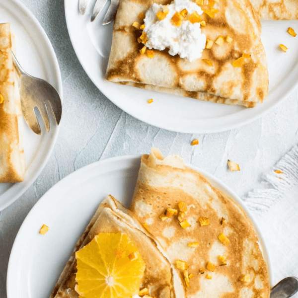 Crepes with whipped cream and orange slices on white plates.