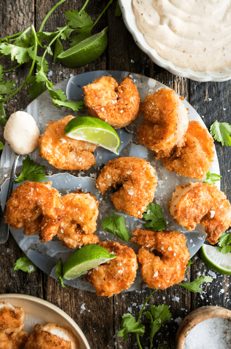 Crispy coconut shrimp with lime, cilantro, and creamy dipping sauce on a wooden table.