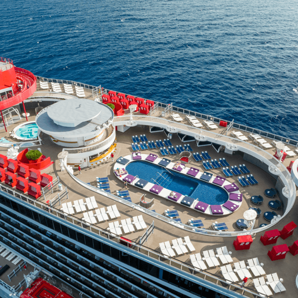 Cruise ship deck with pools, lounge chairs, and red accents sailing on open sea.