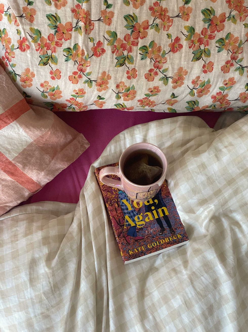 Cup of tea on a book on a floral bed with cozy sheets and pillows.