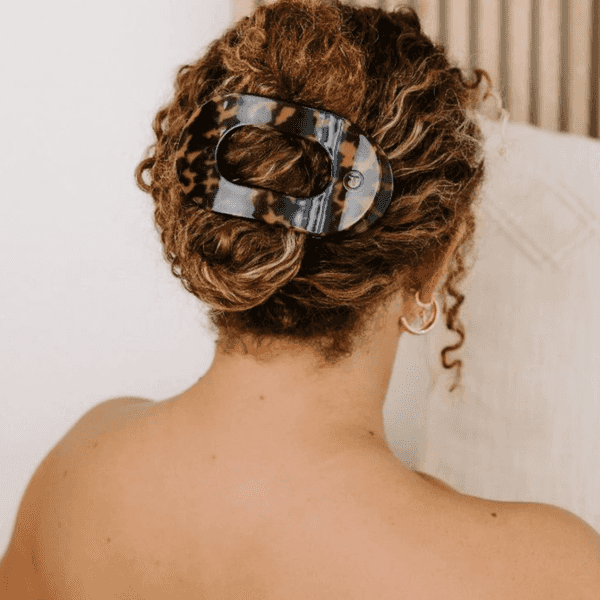 Curly hair pinned with a tortoiseshell clip, woman wearing hoop earrings.