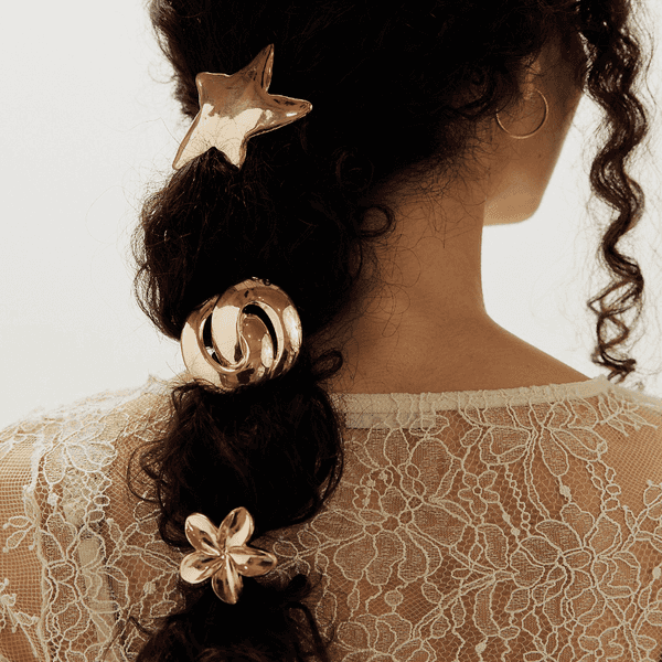 Curly hair styled with gold star, circle, and flower accessories, lace top visible.