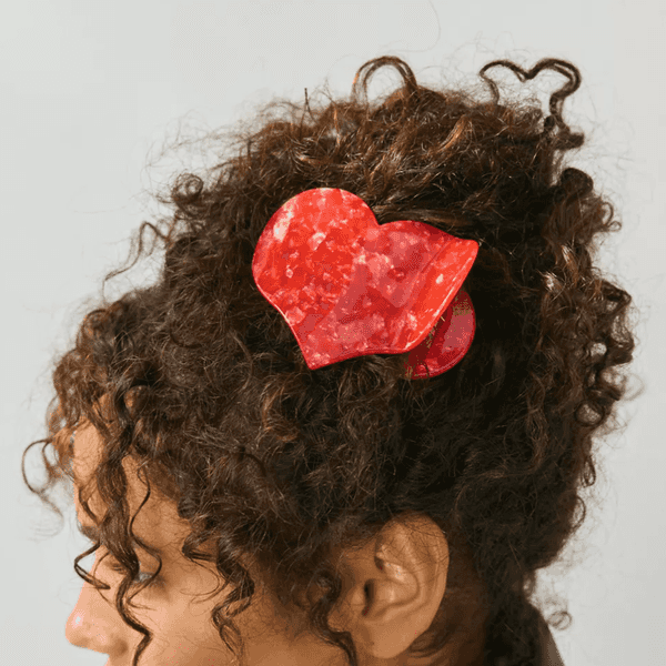 Curly hair with a red, heart-shaped hair clip.