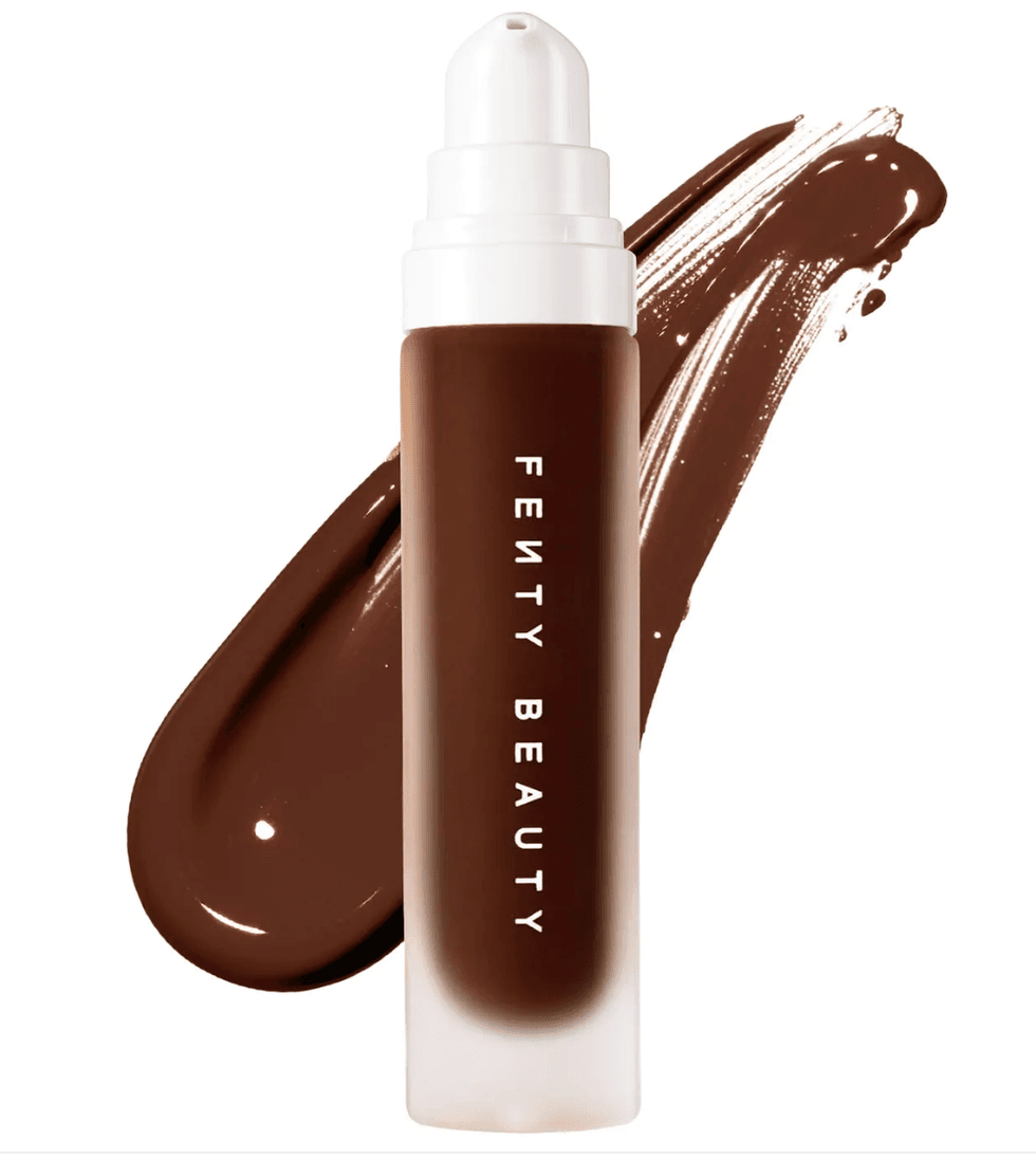 Dark foundation bottle with "Fenty Beauty" label, on a brown smeared background.