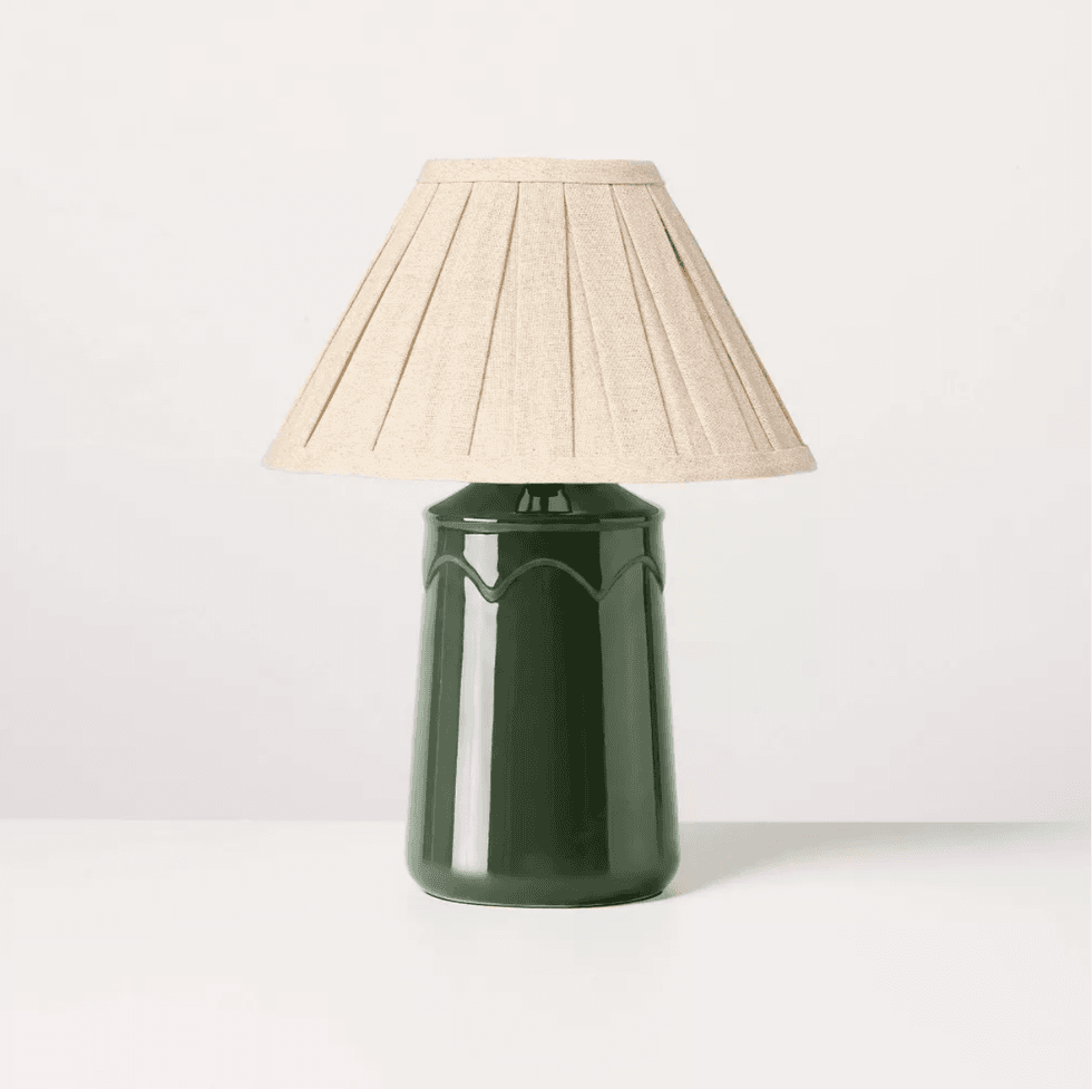 Dark green table lamp with beige pleated shade on white surface.