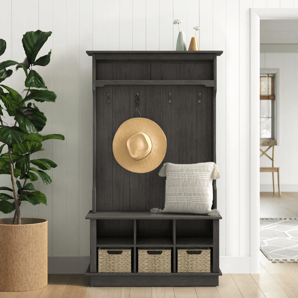 Dark wood hall tree with hat, cushion, and storage baskets beside a potted plant.