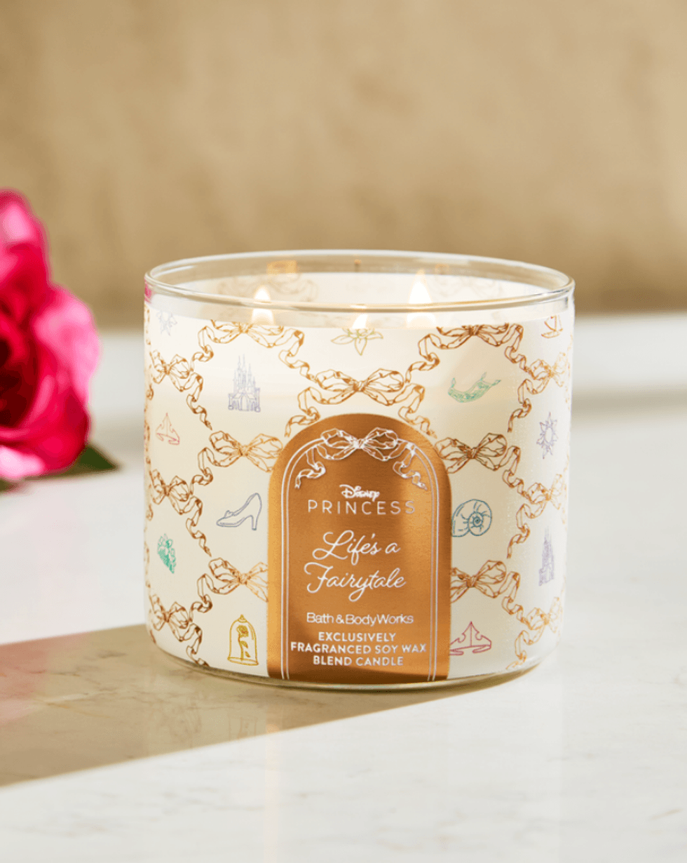 Decorative candle with gold motifs and a pink rose on a marble surface.