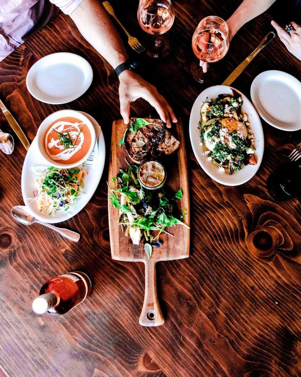 Dinner table with appetizers, salads, bread, and glasses of ros\u00e9 wine on a wooden surface.