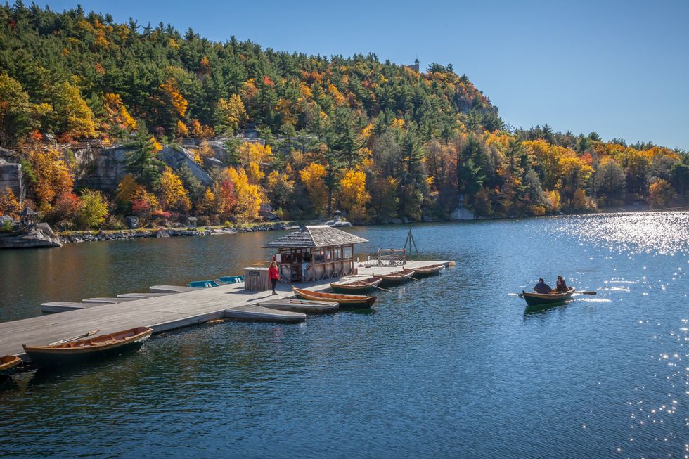 Dock and boats on a lake, surrounded by colorful autumn trees and clear blue skies.