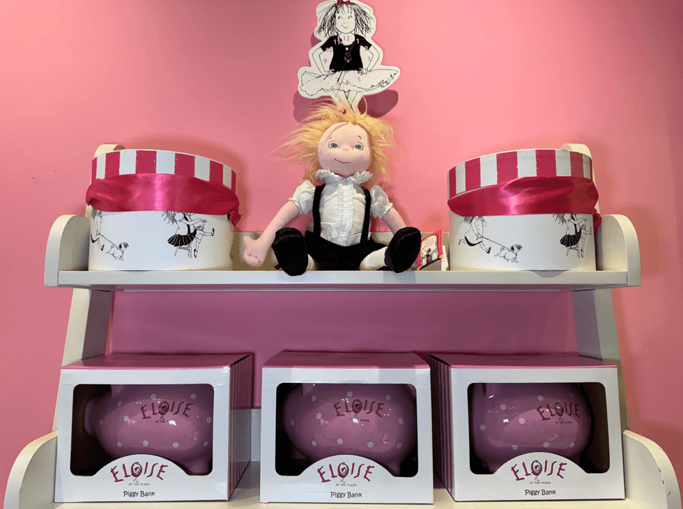 Doll and piggy banks on a shelf with pink and white striped boxes on a pink background.