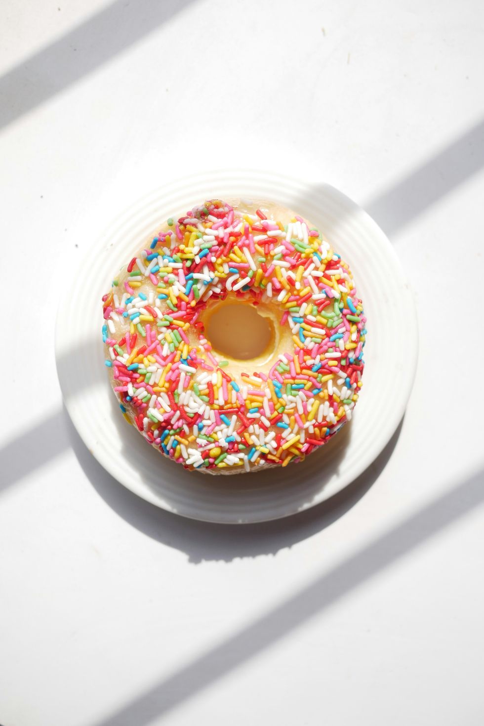 Donut with colorful sprinkles on a white plate in bright sunlight.