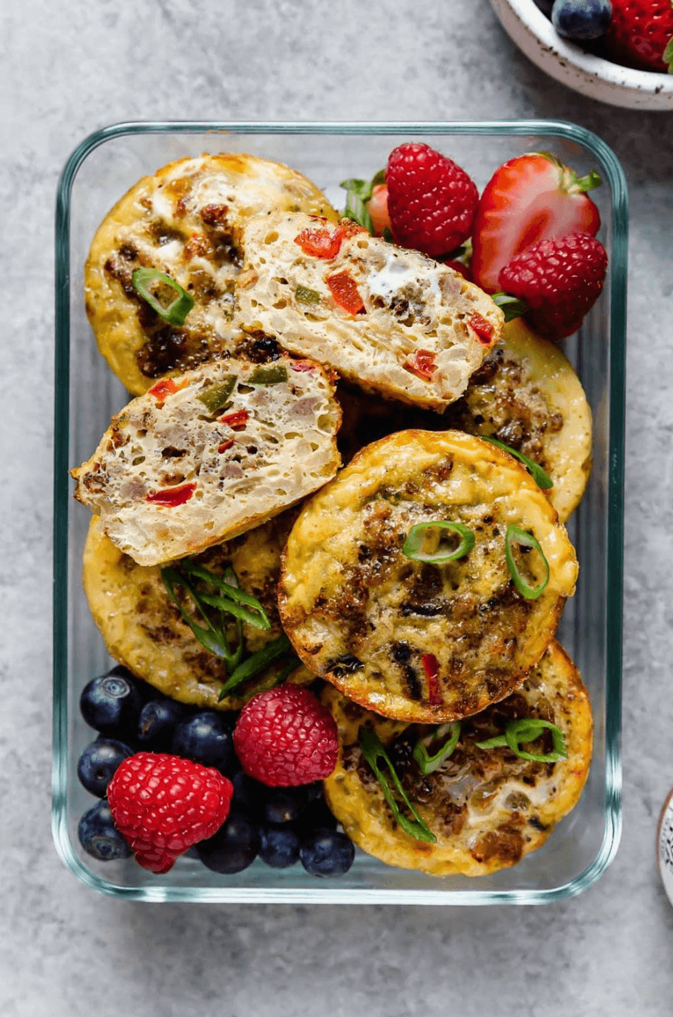 Egg muffins with vegetables and berries in a glass container.